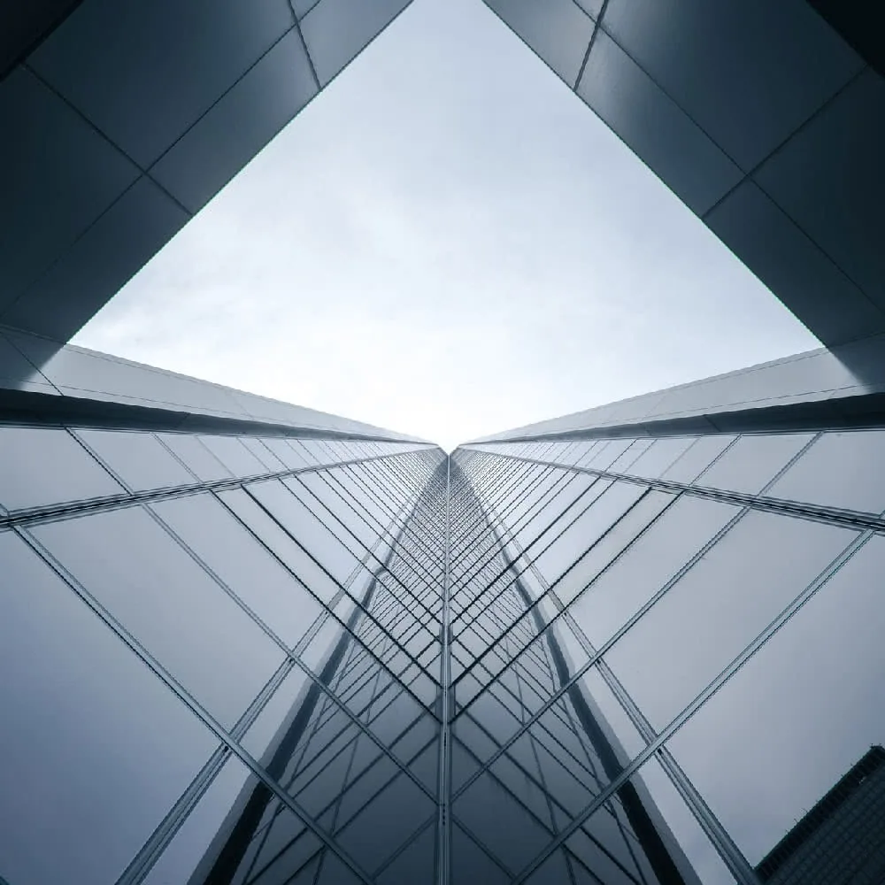 Symmetrical upward view of modern glass and steel building facade converging toward bright sky