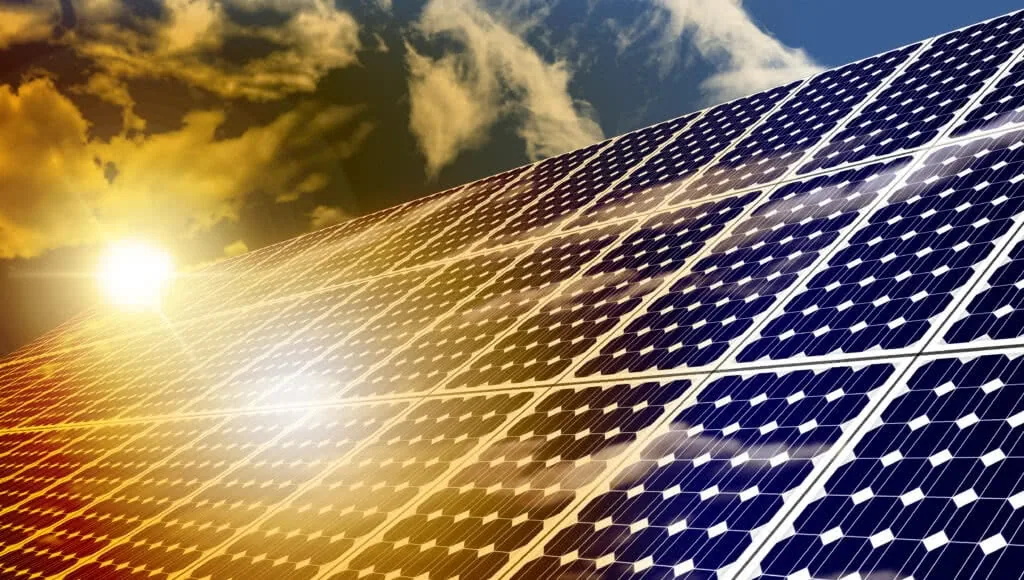 Solar panels at sunset with bright sunlight reflecting off photovoltaic cells against blue sky with clouds